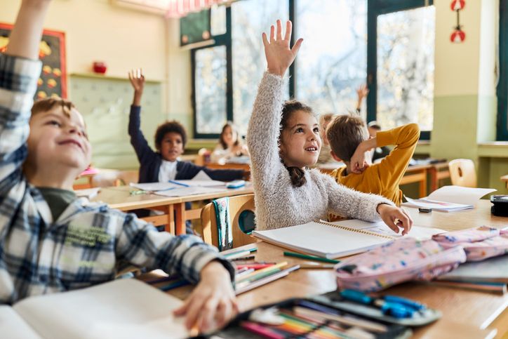 children in classroom raising their hands